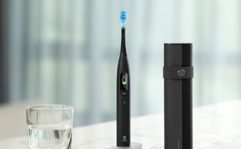 Cepillo de dientes eléctrico negro sentado en un mostrador de mármol junto a un vaso de agua y una caja de transporte negro