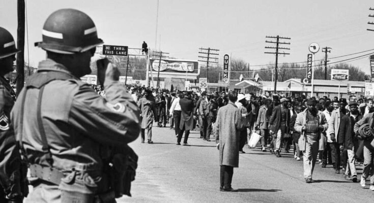 Los soldados están viendo caminar a los manifestantes de derechos civiles durante la tercera marcha de Selma en Alabama el 25 de marzo de 1965. El presidente Lyndon Johnson federalizó a la Guardia Nacional de Alabama para evitar la violencia contra los caminantes.