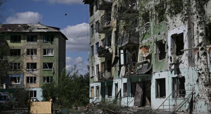 Los residentes usan hojas de madera contrachapada para cubrir las ventanas rotas en un edificio residencial que está fuertemente dañado después de una huelga rusa en la ciudad de Bilozerske, en la región de Donetsk, el 12 de agosto, en medio de la invasión rusa de Ucrania.