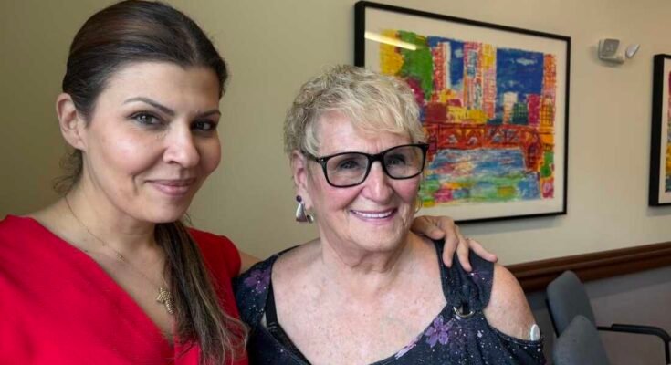 Rachel Nassif tiene su brazo alrededor del hombro Roberta Rabinovitz. Las dos mujeres se paran frente a una pintura colorida y sonriente.